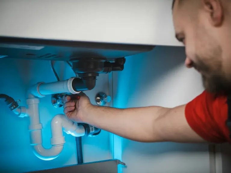 Technician fitting pipework under a kitchen sink